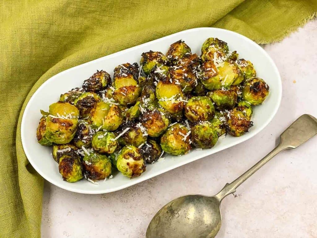 Air fryer Brussels sprouts just cooked on a serving plate with a spoon by the side.