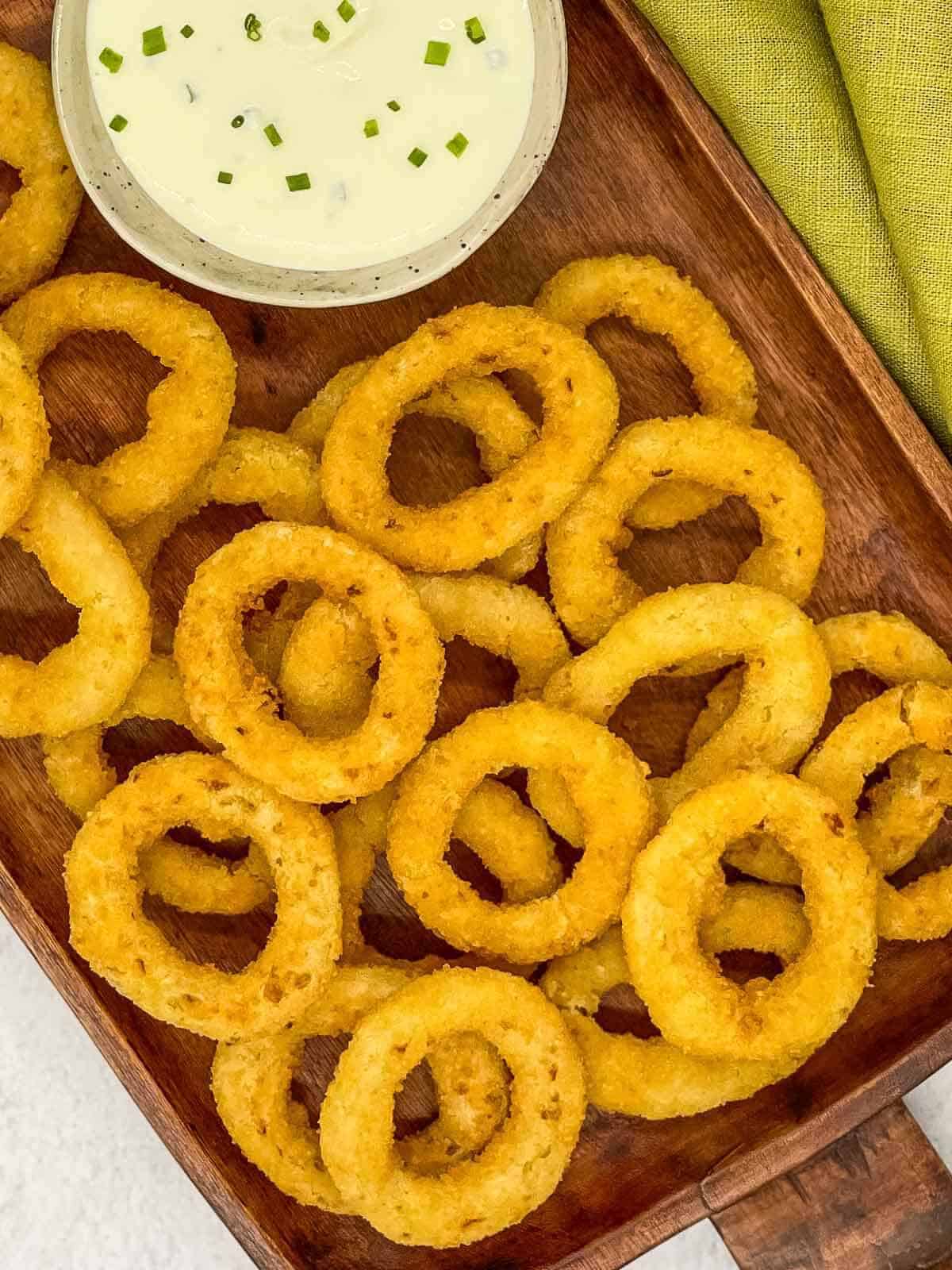 Air fryer frozen onion rings, cooked on a tray with a bowl of sour cream and chive dip.