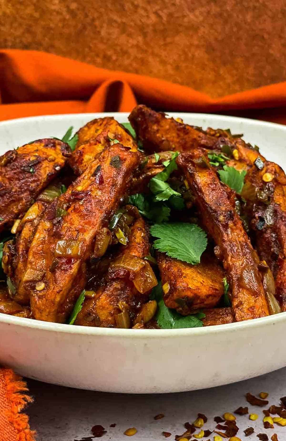 A bowl of hilli potatoes ready to eat with red chili flakes and corinader.