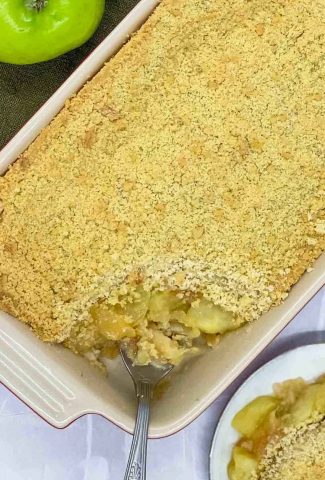 Apple crumble in a baking dish with a portion on a plate and serving spoon in the baking dish.