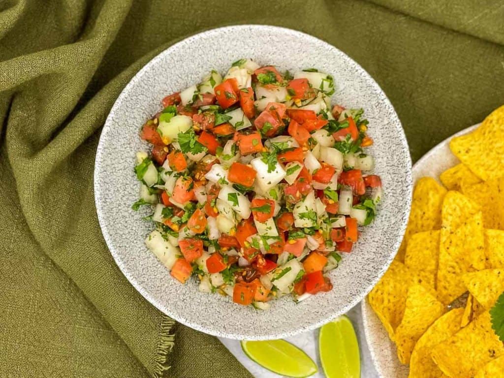 Fresh tomato salsa in a bowl, with lime wedges and tortilla chips.