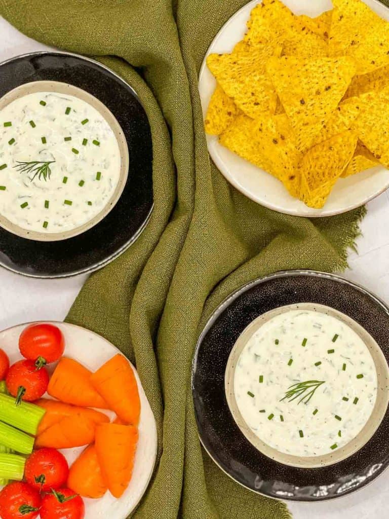 Two bowls of homemade ranch salad dressing, with tortilla chips and fresh vegetables.
