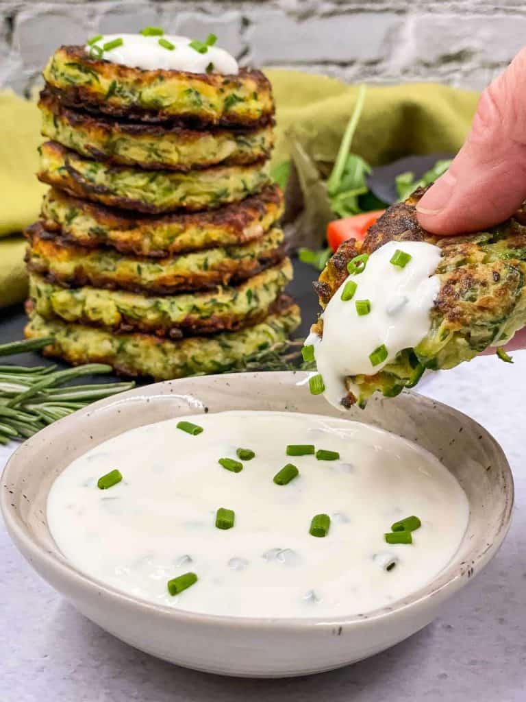 Someone dipping a zucchini fritter into sour cream and chive dipping sauce.