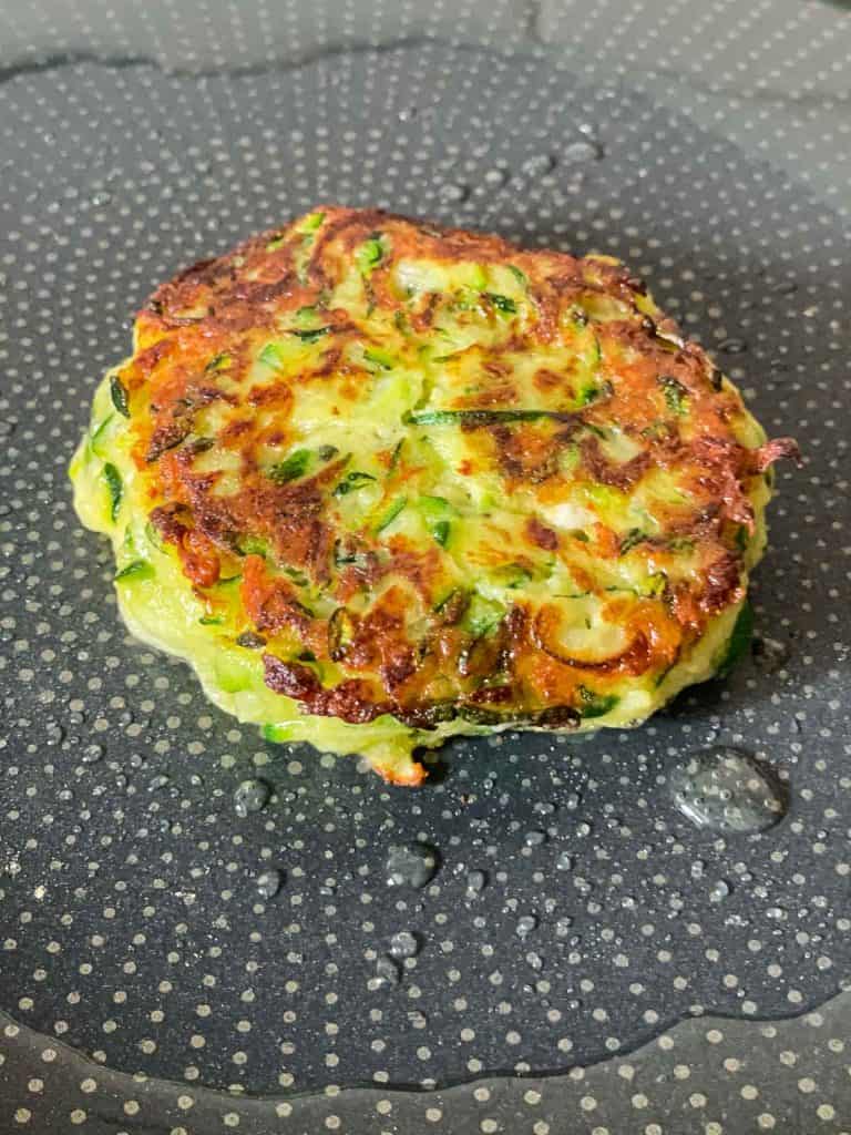 A zucchini fritter cooking in a a skillet.