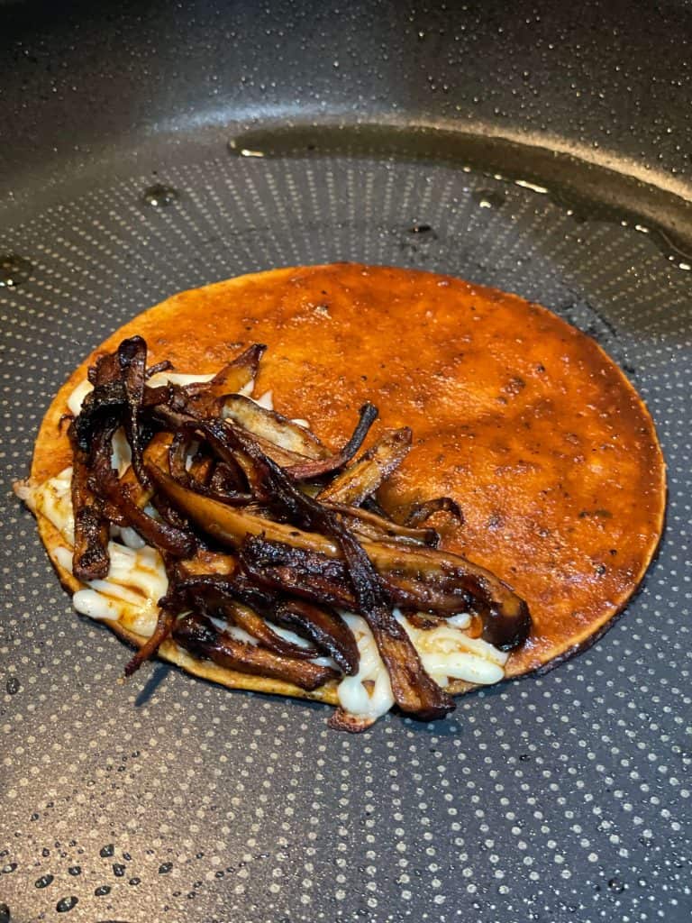 Place vegan cheese and cooked mushrooms on one side of a dipped tortilla.