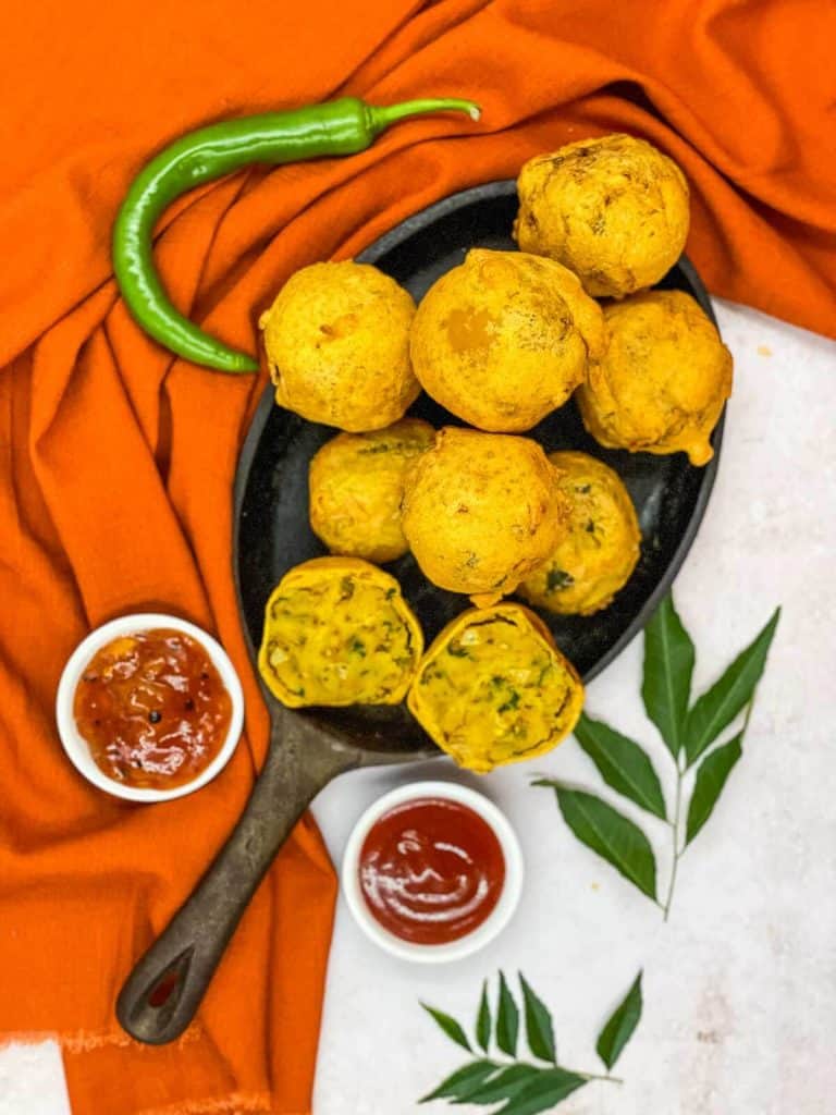 Bonda aloo on a skillet with dipping sauces, green chillies, and curry leaves.