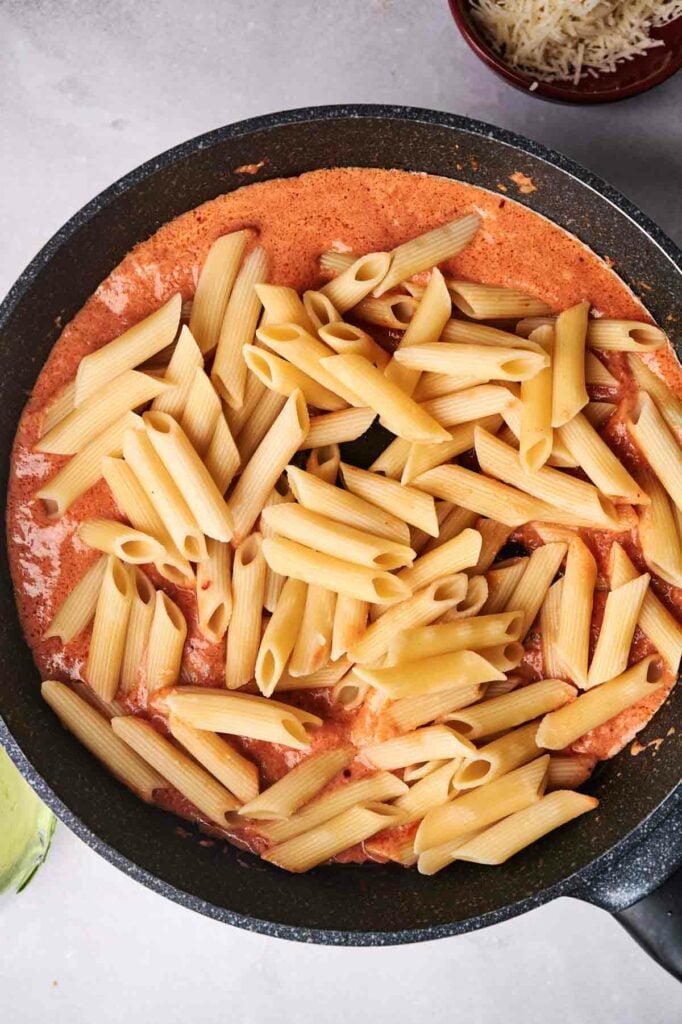 Penne alla vodka in a creamy tomato sauce in a black skillet, with grated cheese on the side.