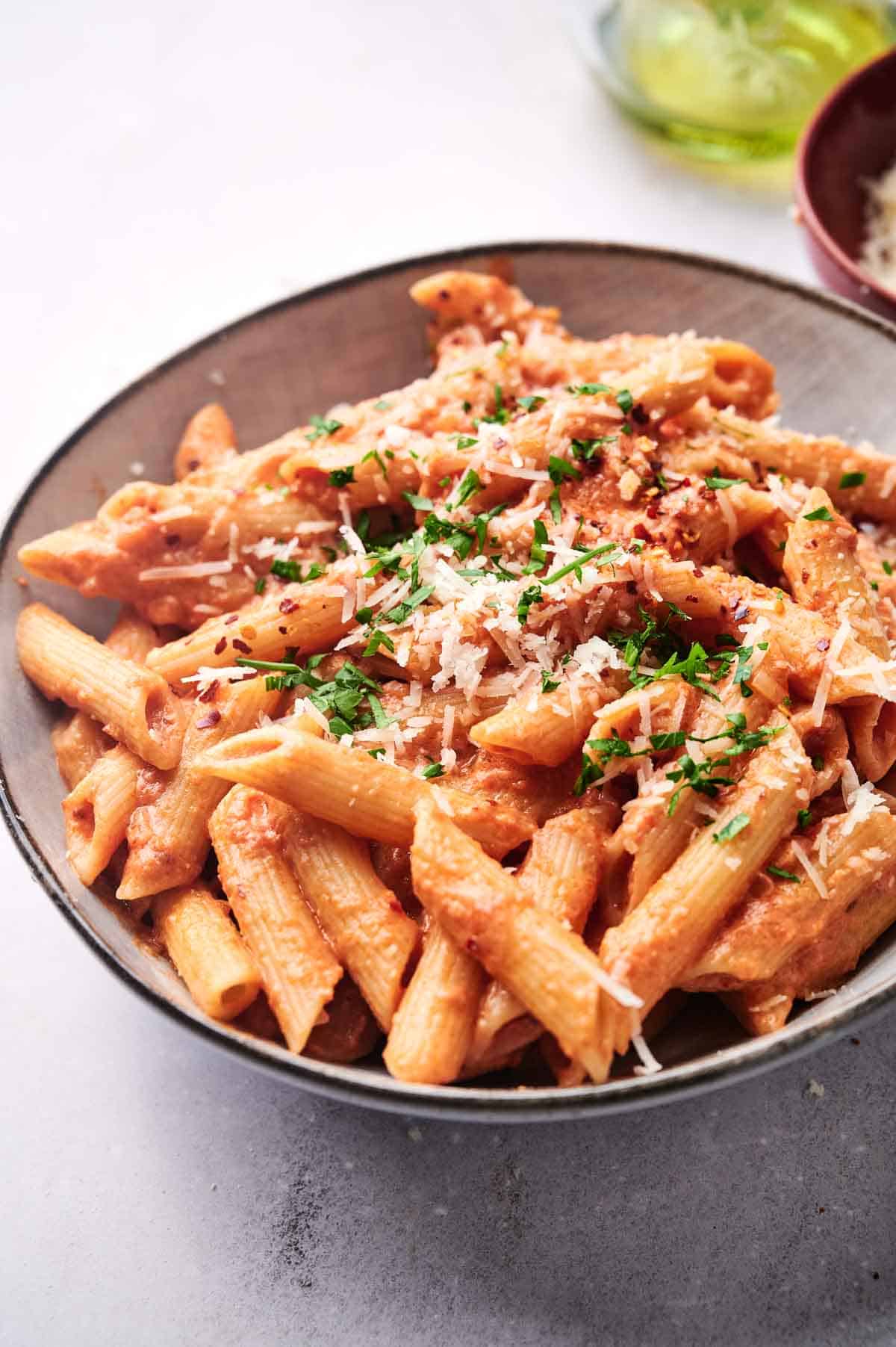 A bowl of penne alla vodka in a creamy tomato sauce, garnished with grated parmesan cheese and chopped herbs.