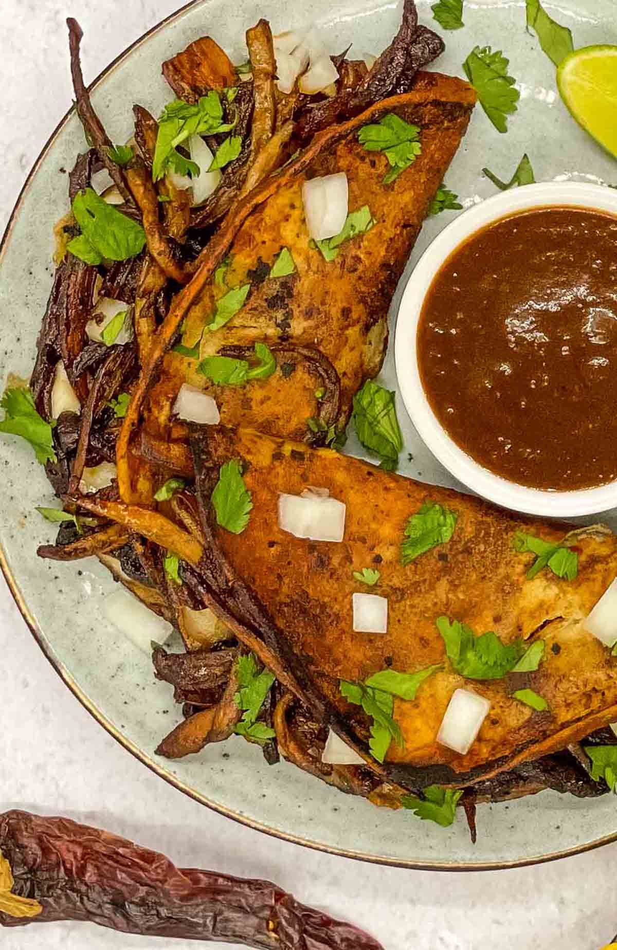 Vegetarian birria tacos on a plate with comsome sauce.