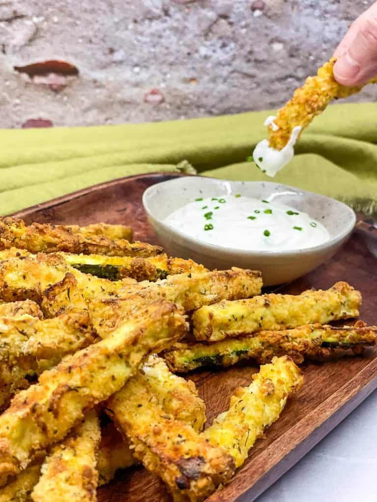 Someone dipping air fried zucchini fries into sour cream.