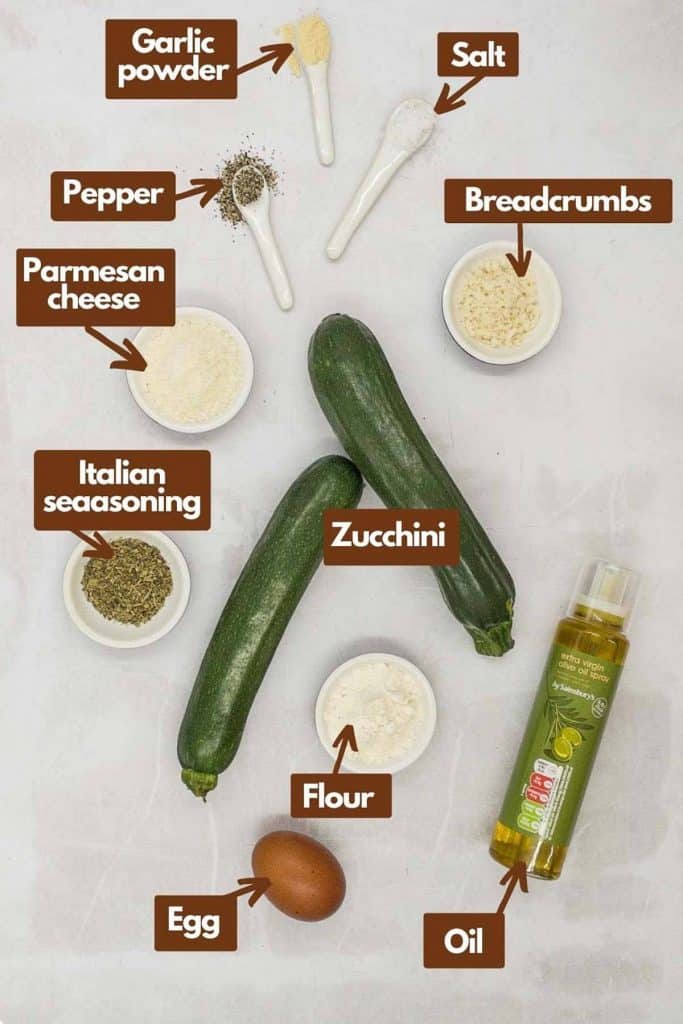 Ingredients needed, garlic powder, salt, bread crumbs, pepper, Parmesan cheese, Italian seasoning, zucchini, flour, olive oil, and egg.
