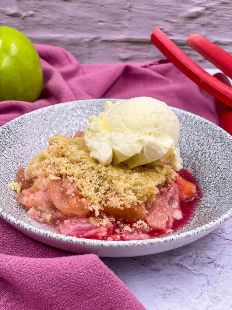 A delicious bowl of tasty crumble with a scoop of ice cream, and rhubarb and an apple.