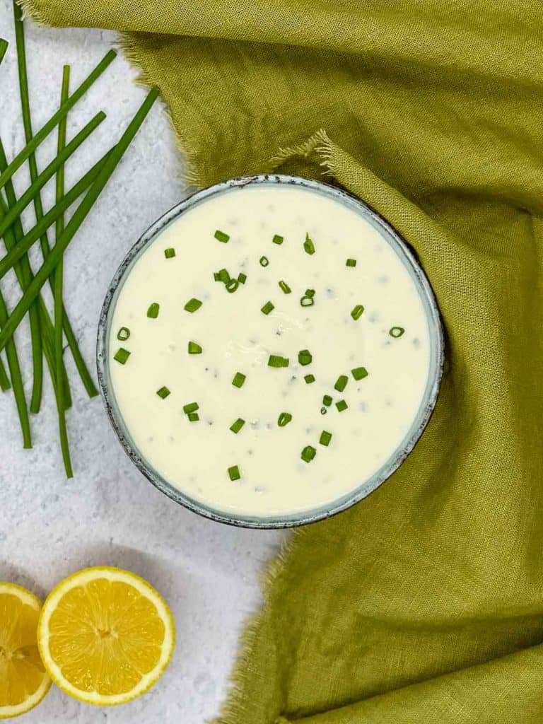 A bowl of sour cream and chives dressing, a fresh lemon, and chives.