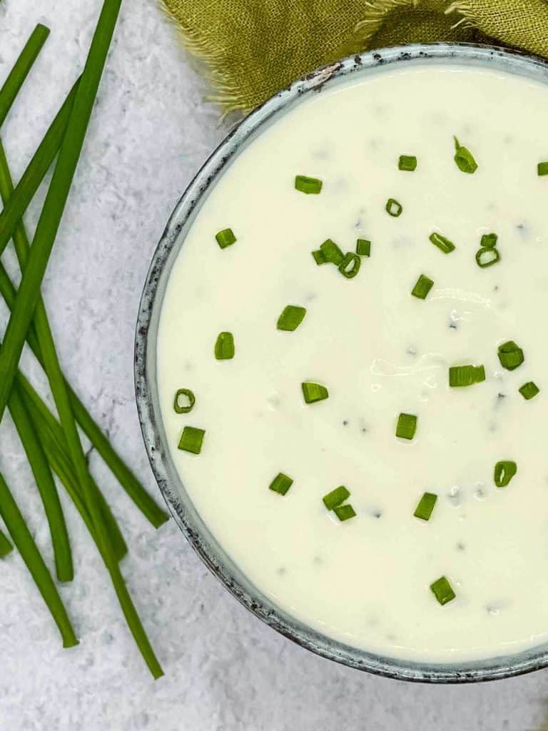 A bowl of tasty sour cream and chives dip, with cut up chives scattered on top.