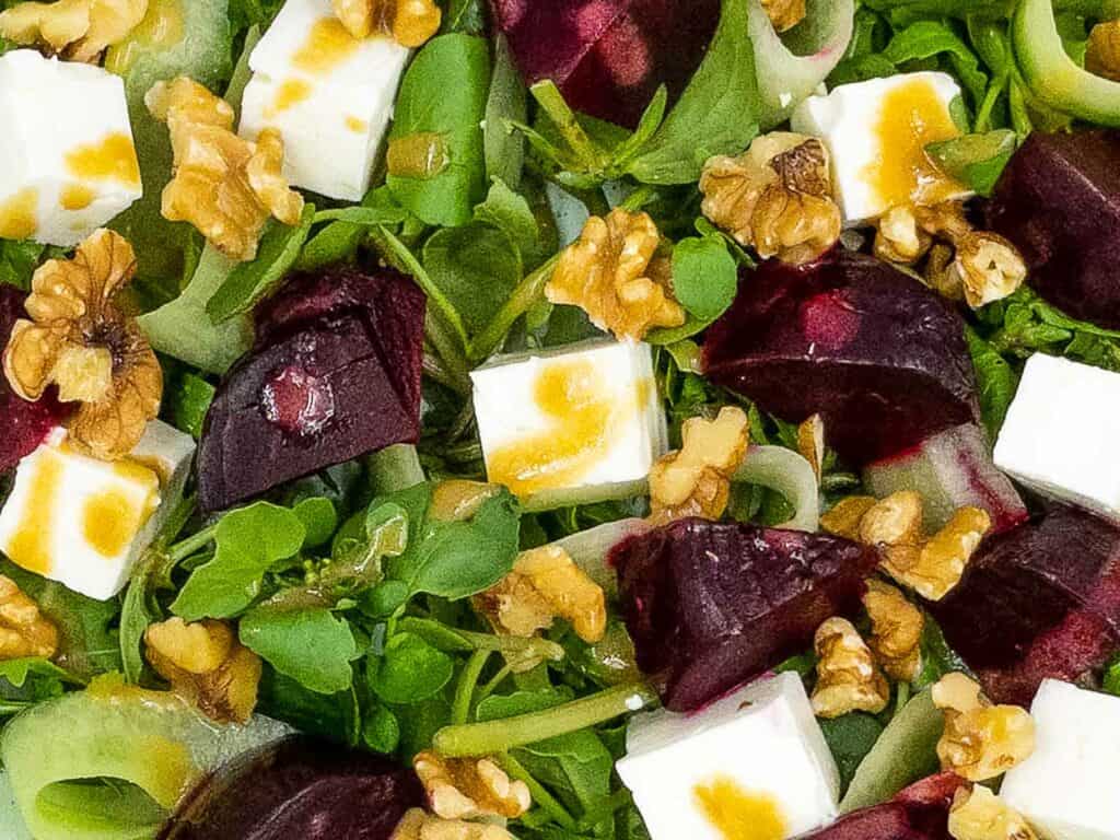 Roasted beetroot, rocket, watercress, feta cheese, and chopped walnuts with a vinaigrette dressing over it.