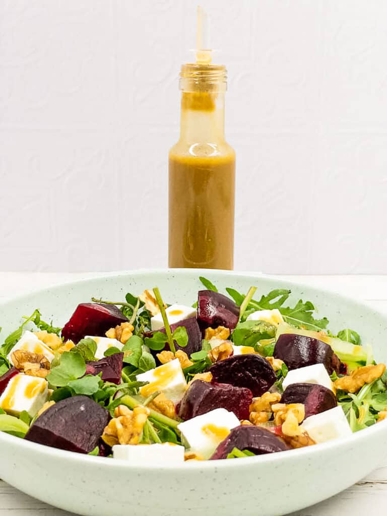 Roasted beetroot salad in a bowl with a bottle of dressing behind it.