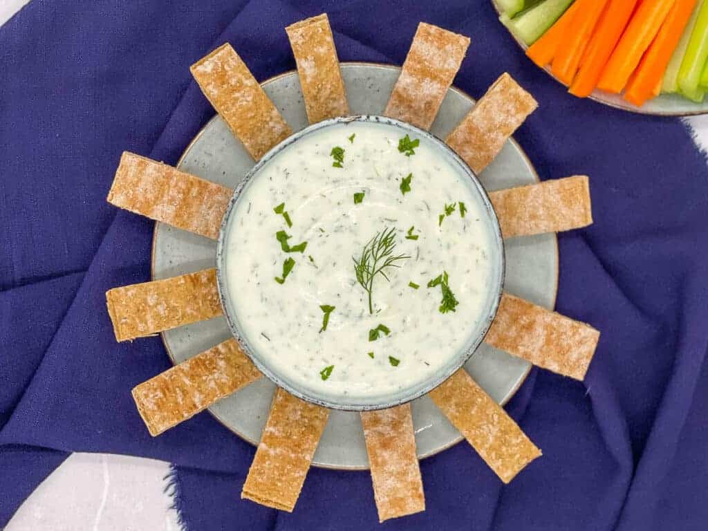 Turkish yogurt dip in a bowl with chopped mint, and fresh dill, with pita bread and raw vegetables.