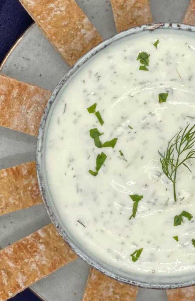 Haydari yogurt dip in a bowl with pita bread around it.