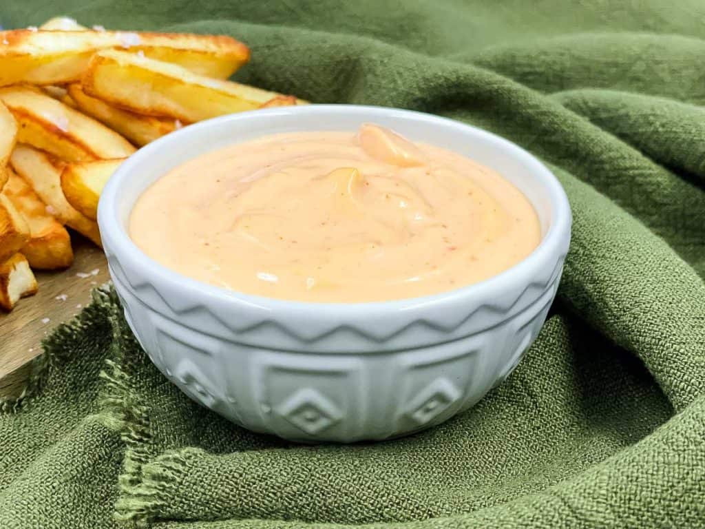 A bowl of homemade sriracha aioli with some French fries behind it.