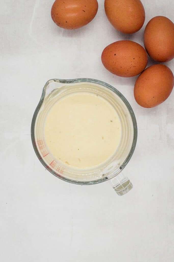 Gluten free Yorkshire pudding batter in a jug, with eggs by the side.