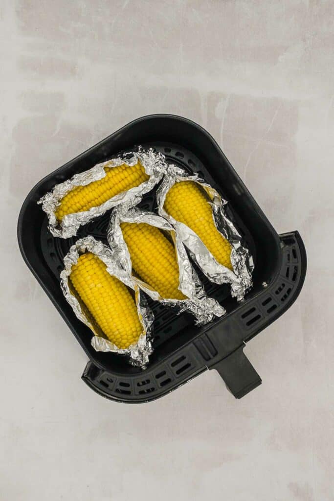 Corn on the cob wrapped in foil in an air fryer basket.