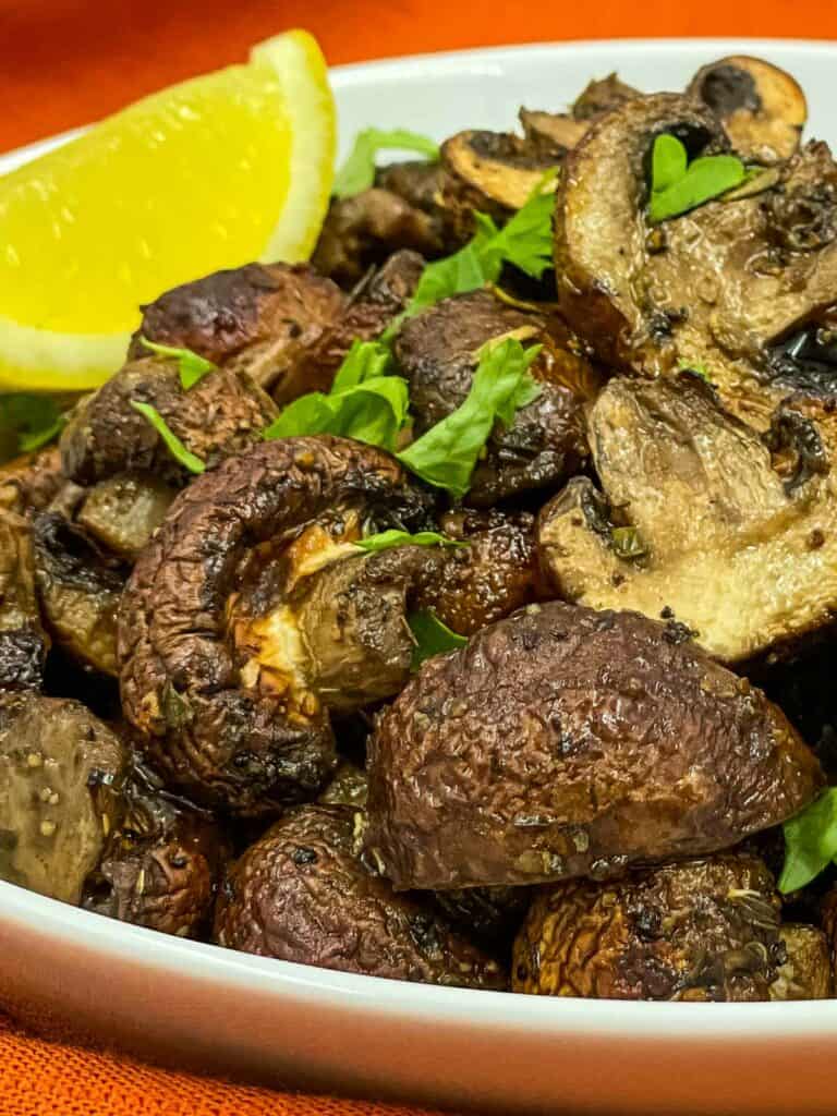 A bowl with air fryer mushrooms with fresh parsley and a lemon wedge.