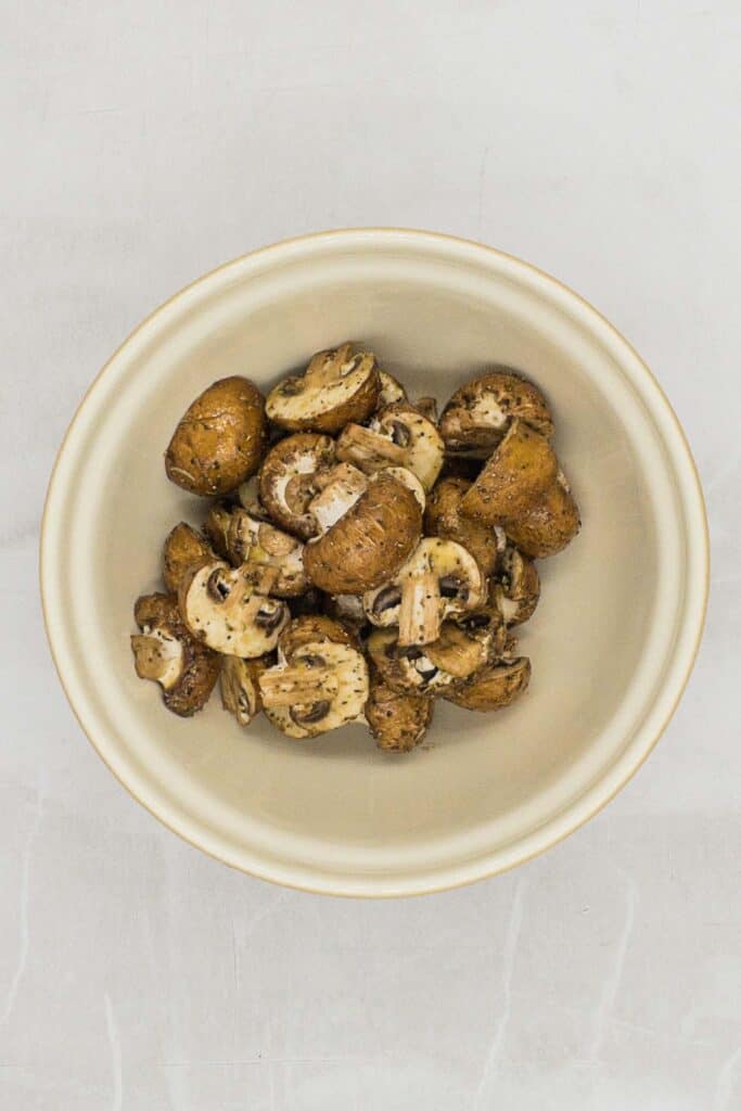 Mushrooms in a bowl with seasoning and olive oil on them.