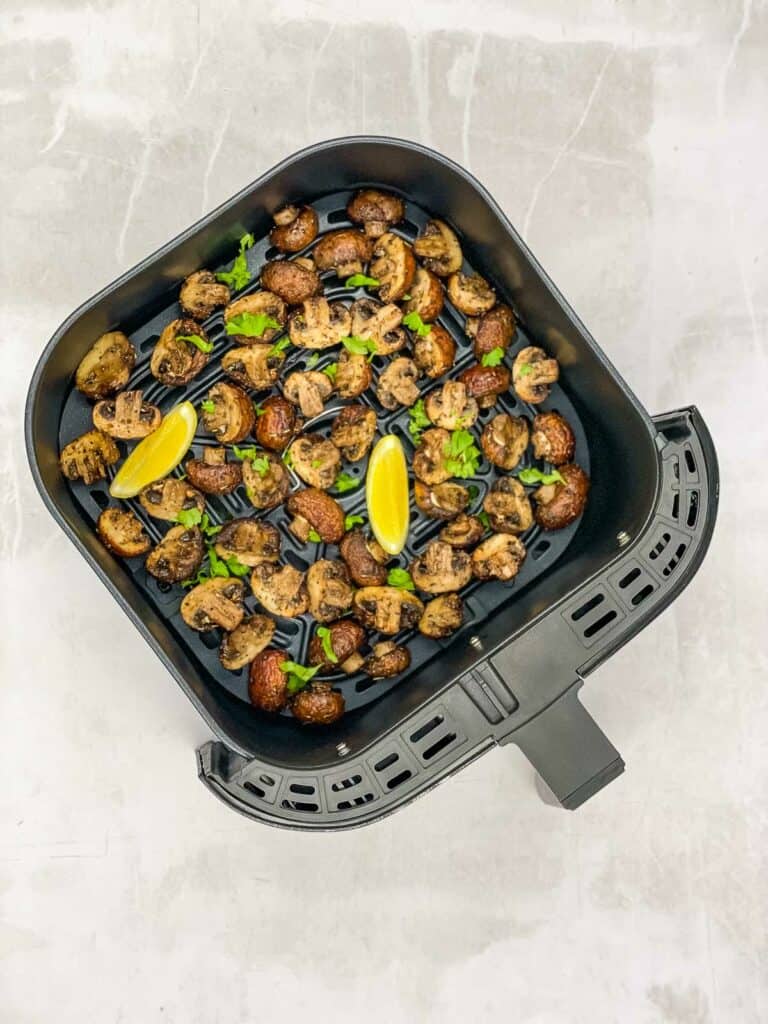An air fryer basket with cooked mushrooms and lemon wedges.