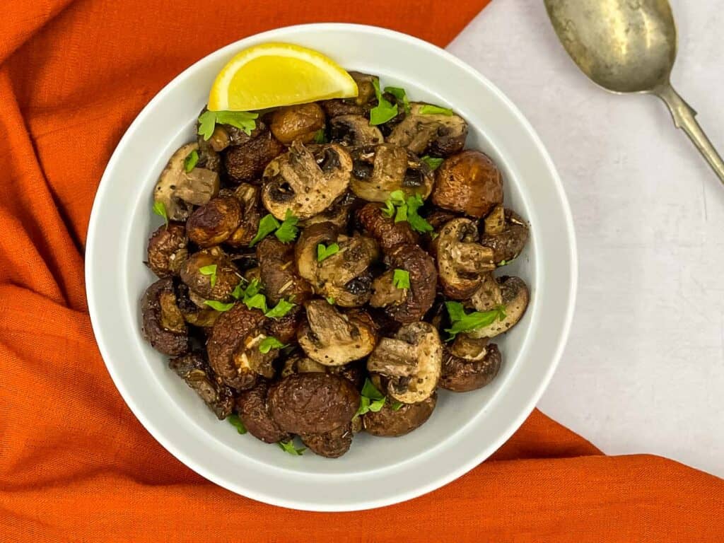 A big bowl of freshly made mushrooms from the air fryer, a lemon wedge and a serving spoon.