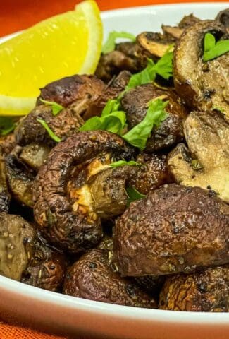 Delicious air fryer mushrooms in a bowl with a lemon wedge.