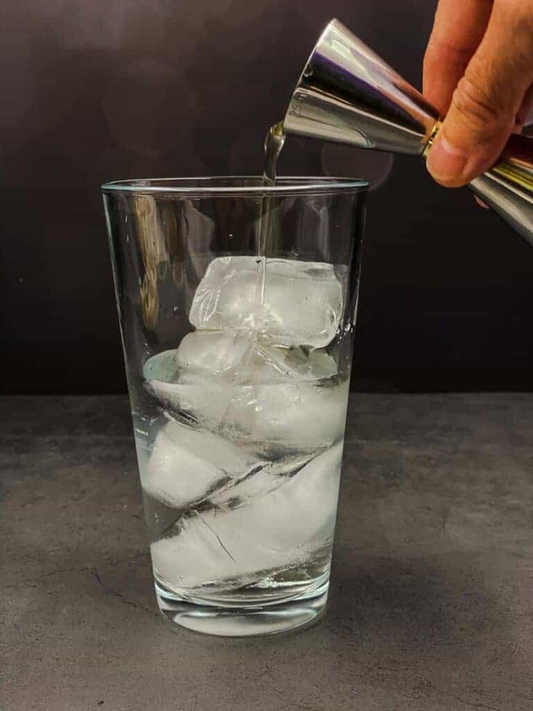 Someone pouring olive juice into a cocktail mixing glass filled with ice, vodka and vermouth.