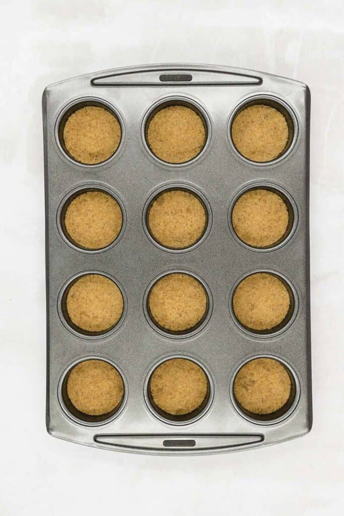Muffin tin with the biscuit crumb base in each hole.