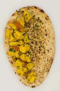 A naan bread with aloo gobi on half of it.