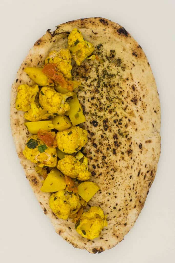 A naan bread with aloo gobi on half of it.