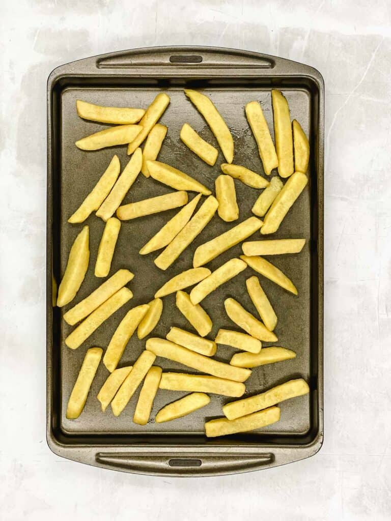 French fries on a baking tray coated with oil.