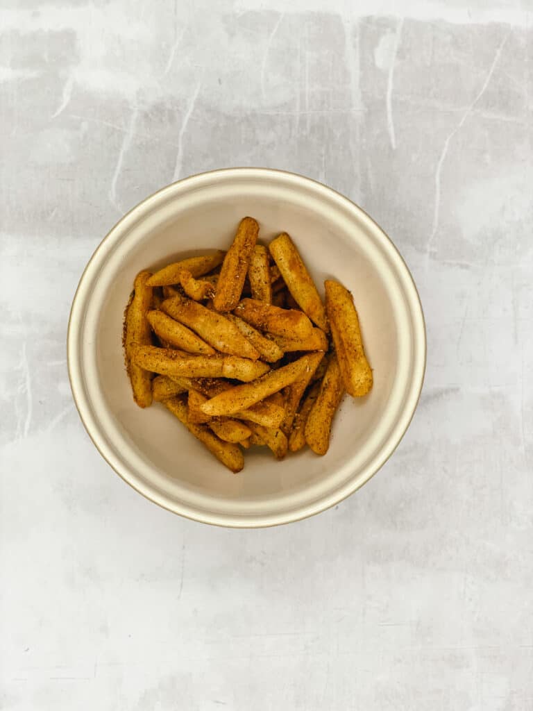 Cooked French fries in a mixing bowl coated with peri peri seasoning.