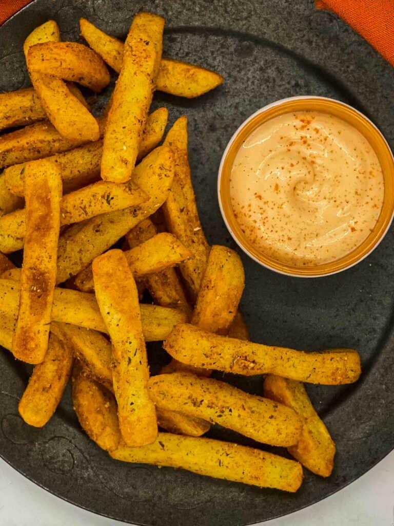 Peri peri fries on a plate with a spicy dip.