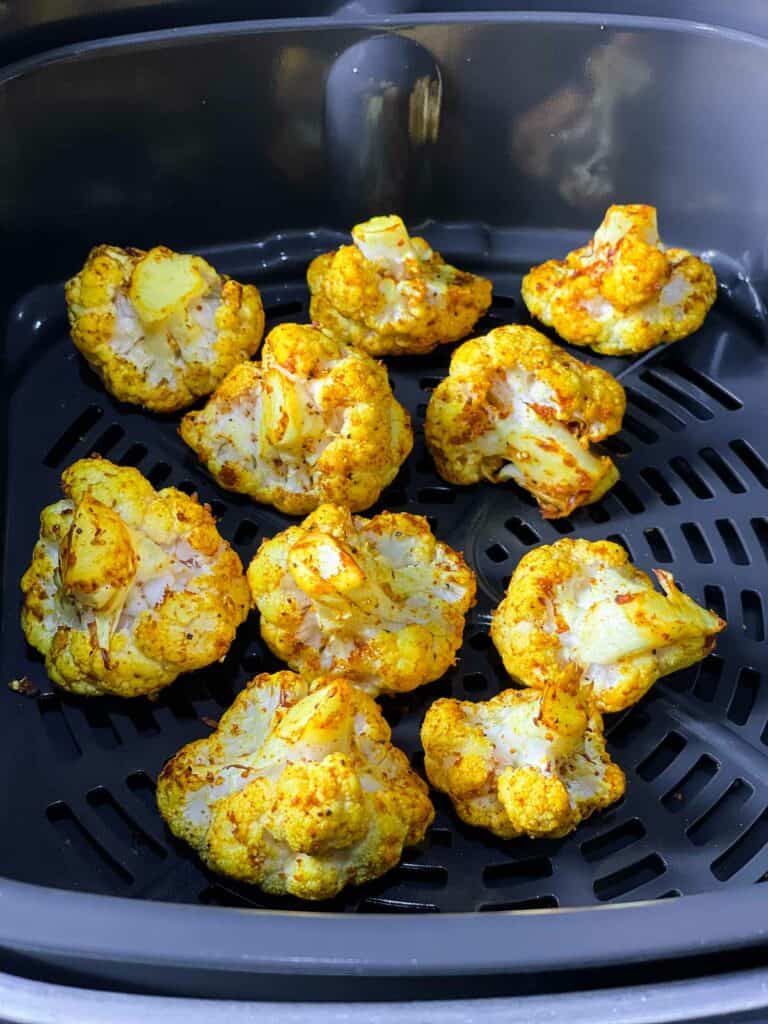 Cauliflower spiced and ready to air fry in an air fryer basket.