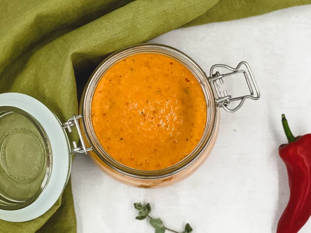 Peri peri sauce in a jar, with fresh oregano and red chili peppers.