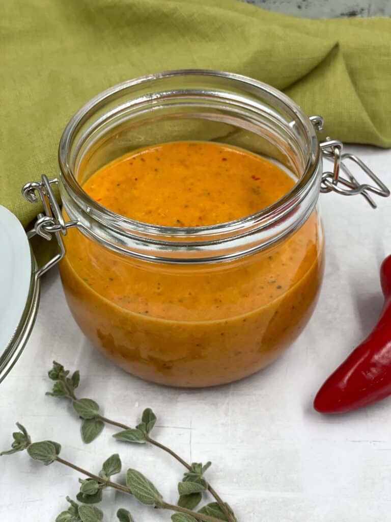 Homemade piri piri sauce n a jar with a red chili pepper and oregano.