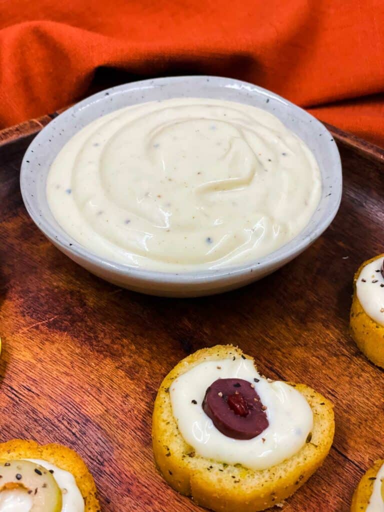 A bowl of homemade pizza aioli on a tray with crostini with aioli on.
