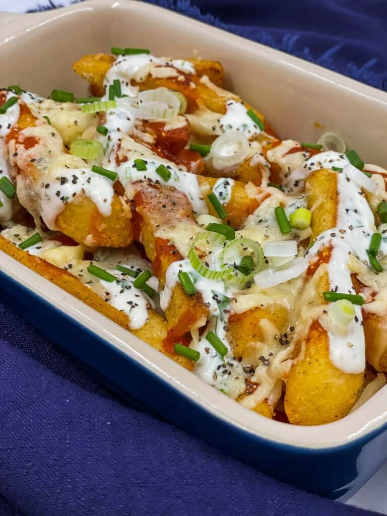 Buffalo fries with buffalo sauce, ranch dressing, scallions and chives in an ovenproof dish.