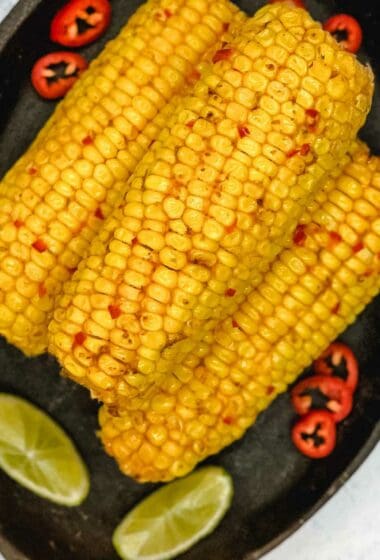 Chili and lime corn on the cob with lime wedges and red chili peppers.