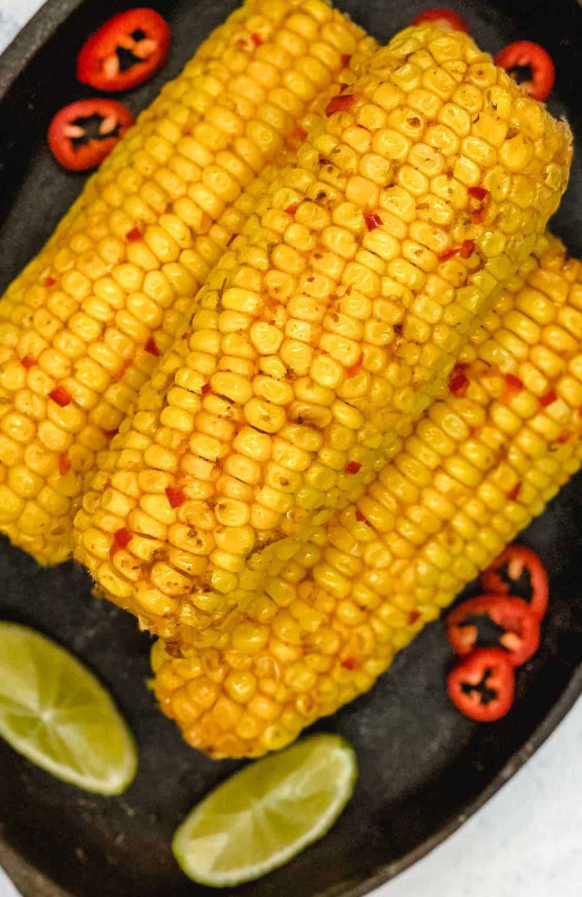 Chili and lime corn on the cob with lime wedges and red chili peppers.