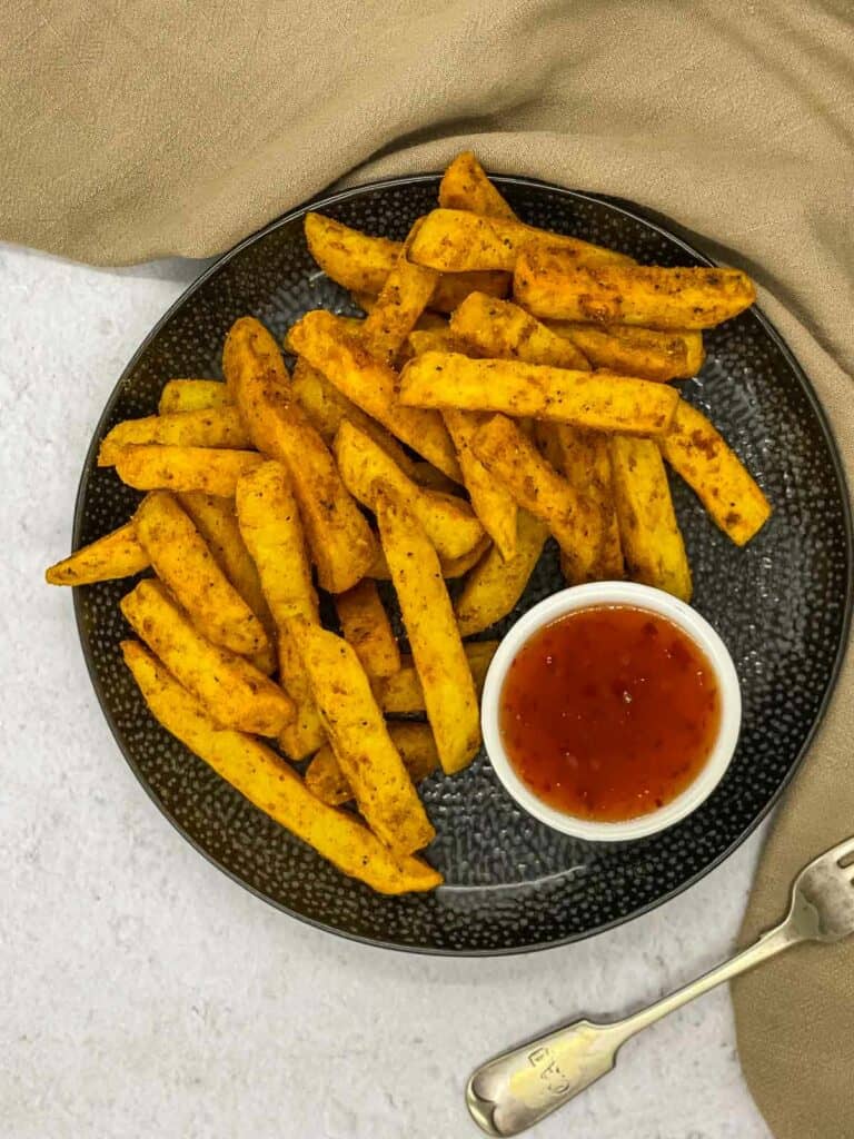 Homemade masala chips on a plate with chilli sauce to dip them in.