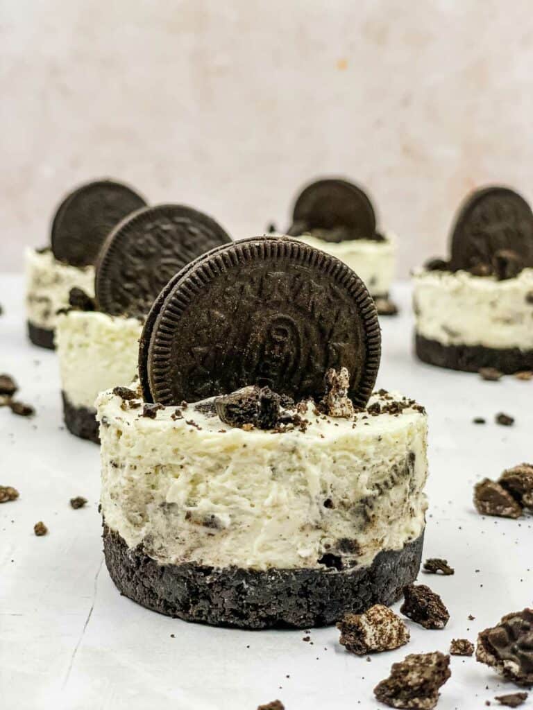 Individual Oreo cheesecakes with Oreo crumbs scattered around.