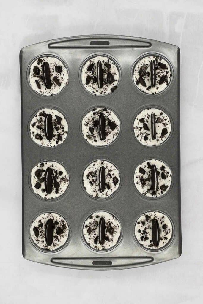 A muffin tray with mini oreo cheesecakes in them.