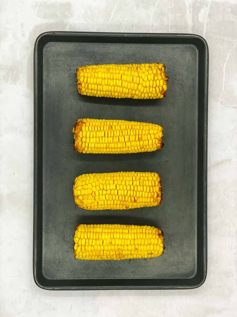 Four sweet corn on the cobs on a baking sheet, cooked.
