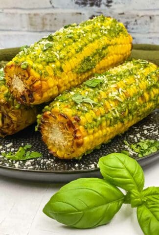 Corn on the cob with pesto butter on a plate.