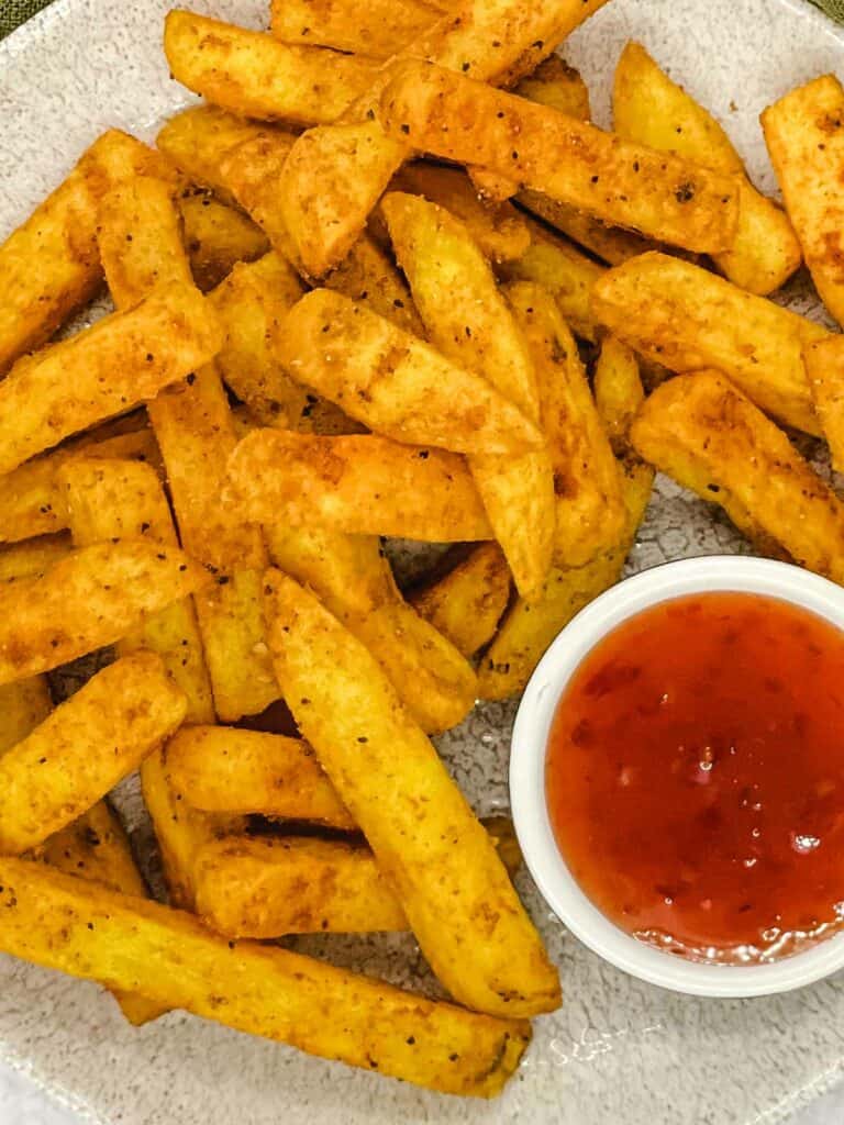 Air fried masala fries on a plate with sweet chili dipping sauce.